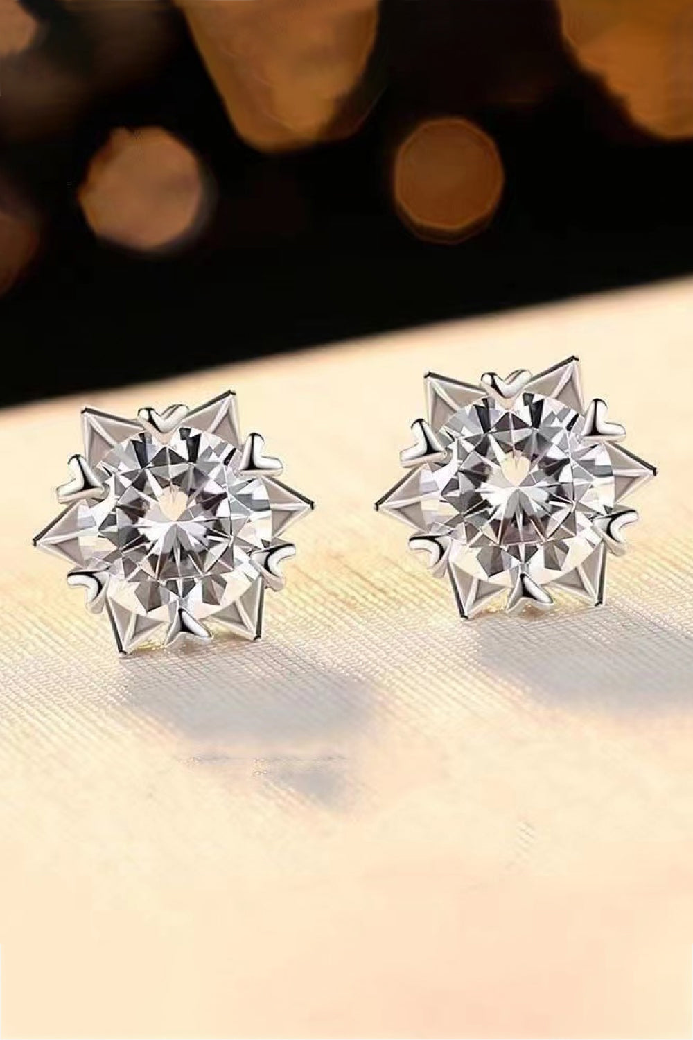 Pair of round clear-stone stud earrings in pointed silver-tone settings on a pale display
