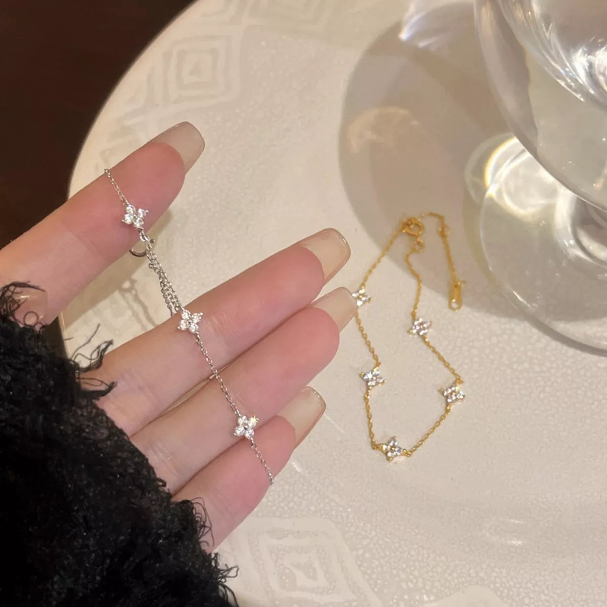 Fine silver charm bracelet draped across a hand beside gold-toned jewelry.