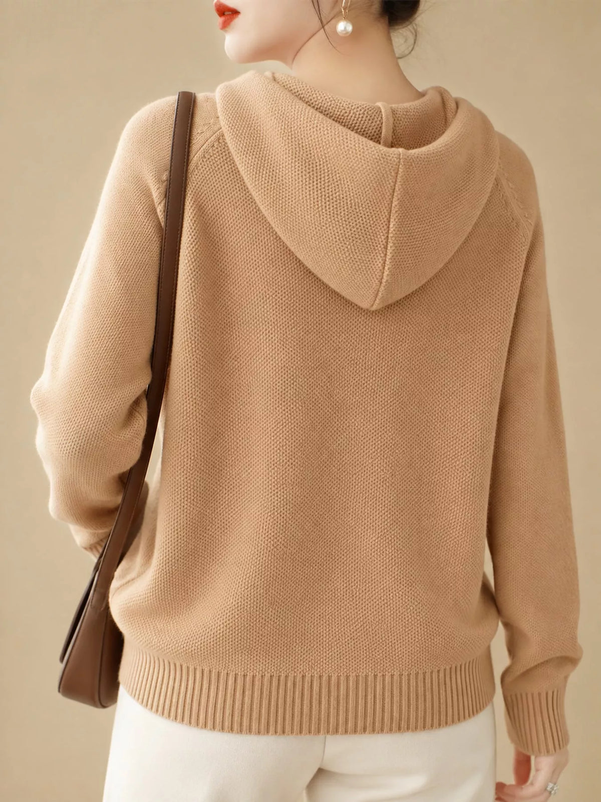 Back view of the camel sweater showing its hood, ribbed hem and brown shoulder bag.