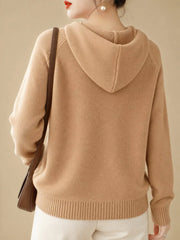 Back view of the camel sweater showing its hood, ribbed hem and brown shoulder bag.