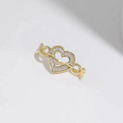 Gold-tone open-heart ring with a crystal outline and looped band on a pale surface