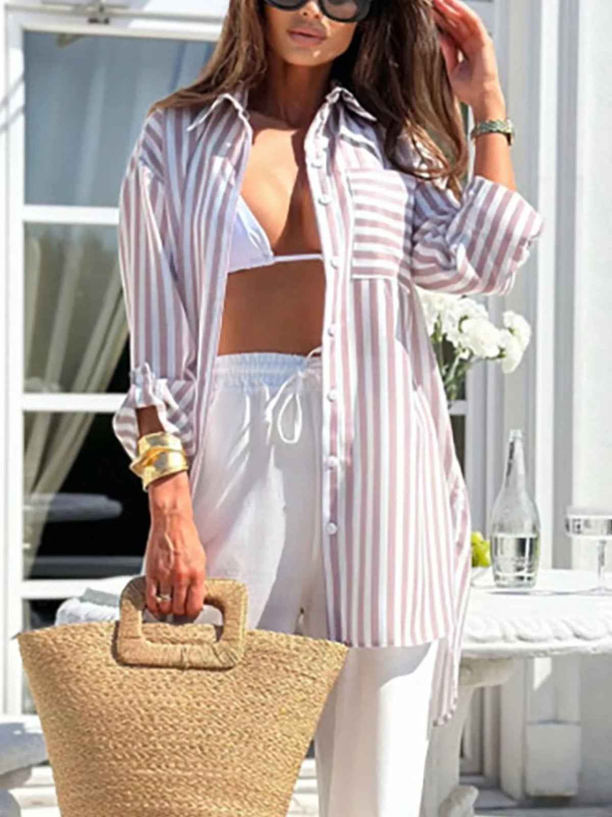 Model wearing blue striped shirt with white trousers and straw handbag.