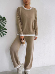 Taupe contrast-trim sweater and pants shown leaning against a wall with a takeaway cup.