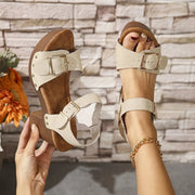 Cream platform sandal held beside a matching worn shoe, showing two buckled straps