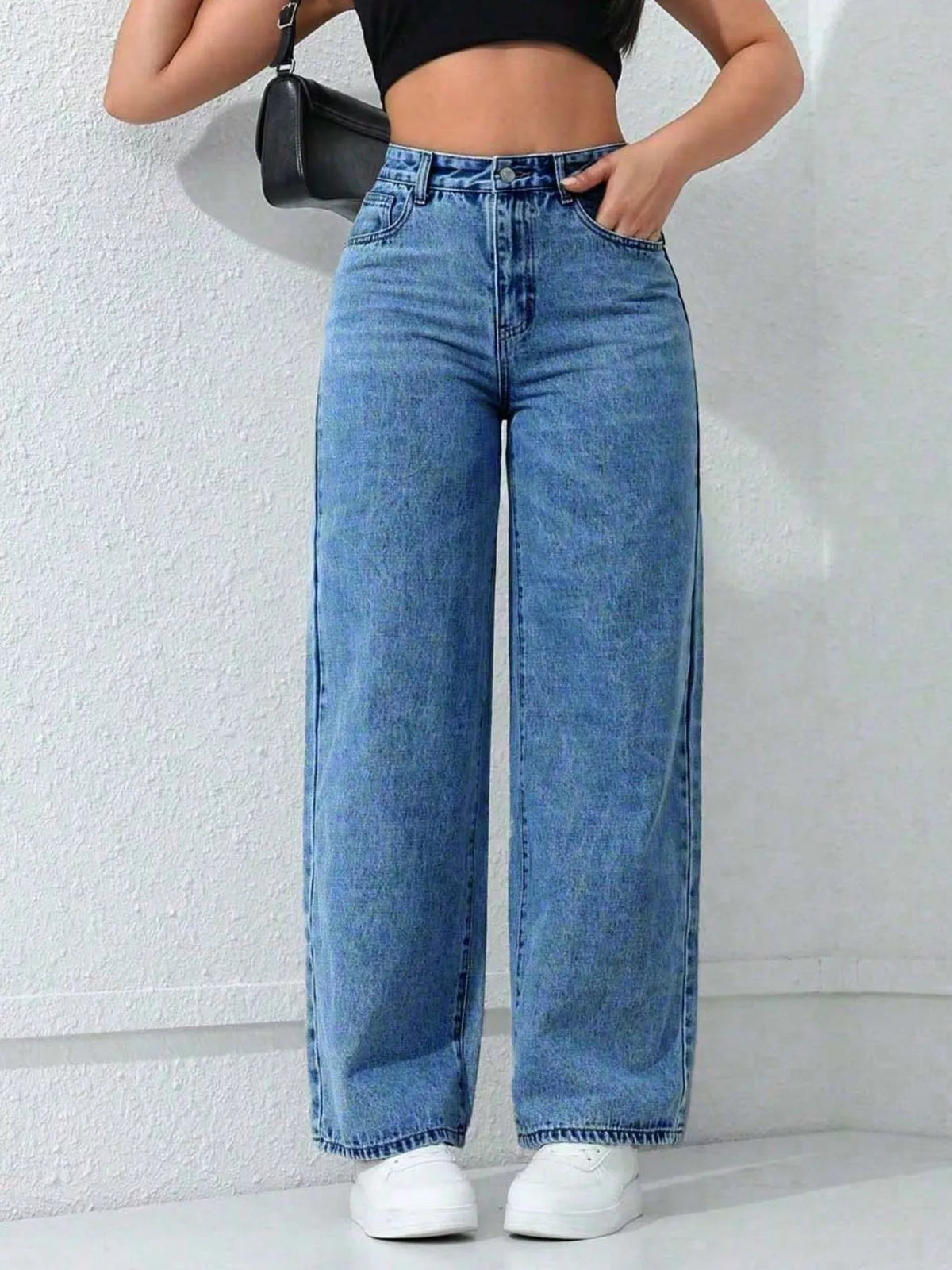 Front view of high-waisted blue wide-leg jeans styled with a black crop top and white trainers