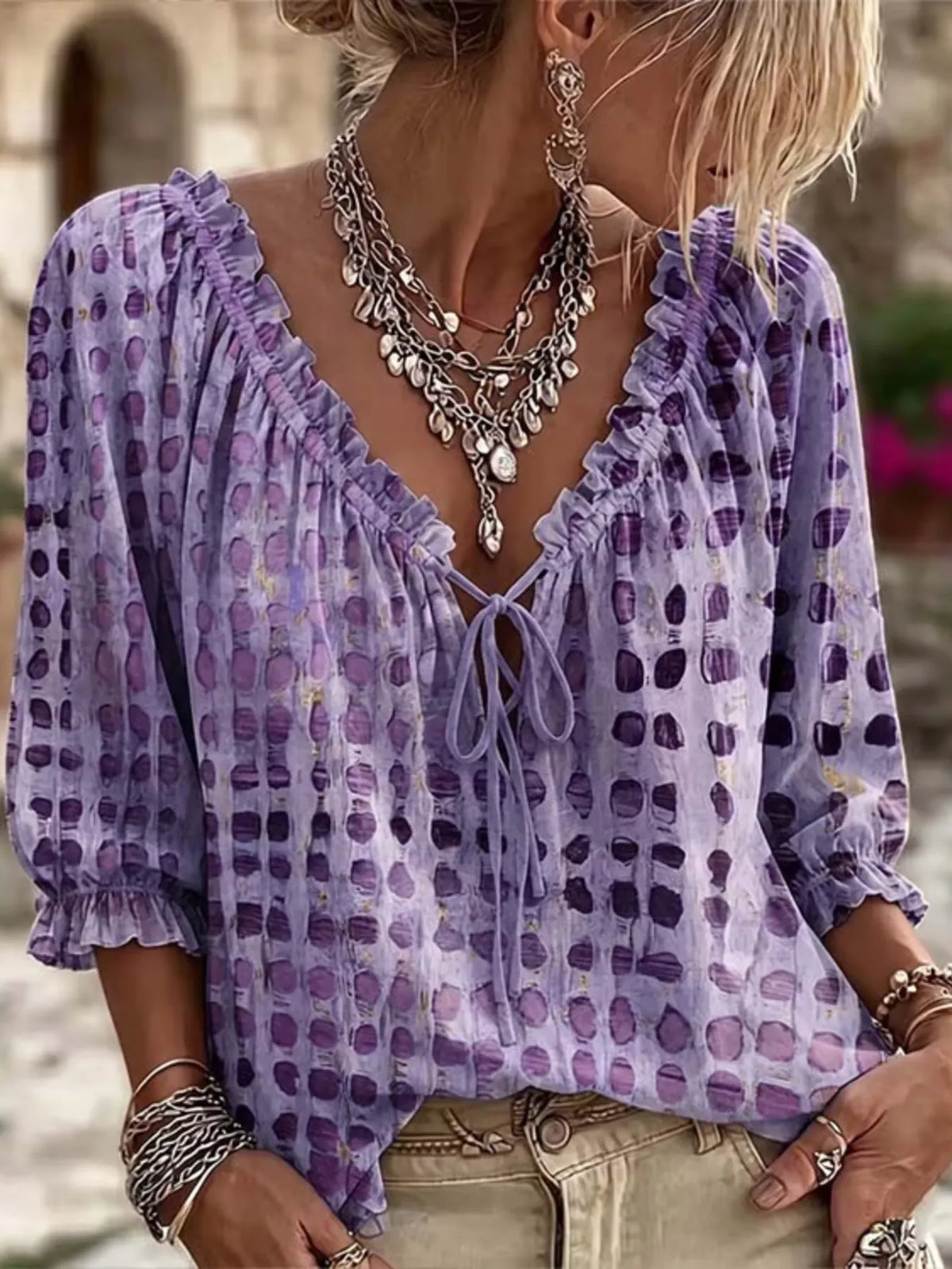 Model wearing a purple spotted blouse with ruffled neckline and three-quarter sleeves