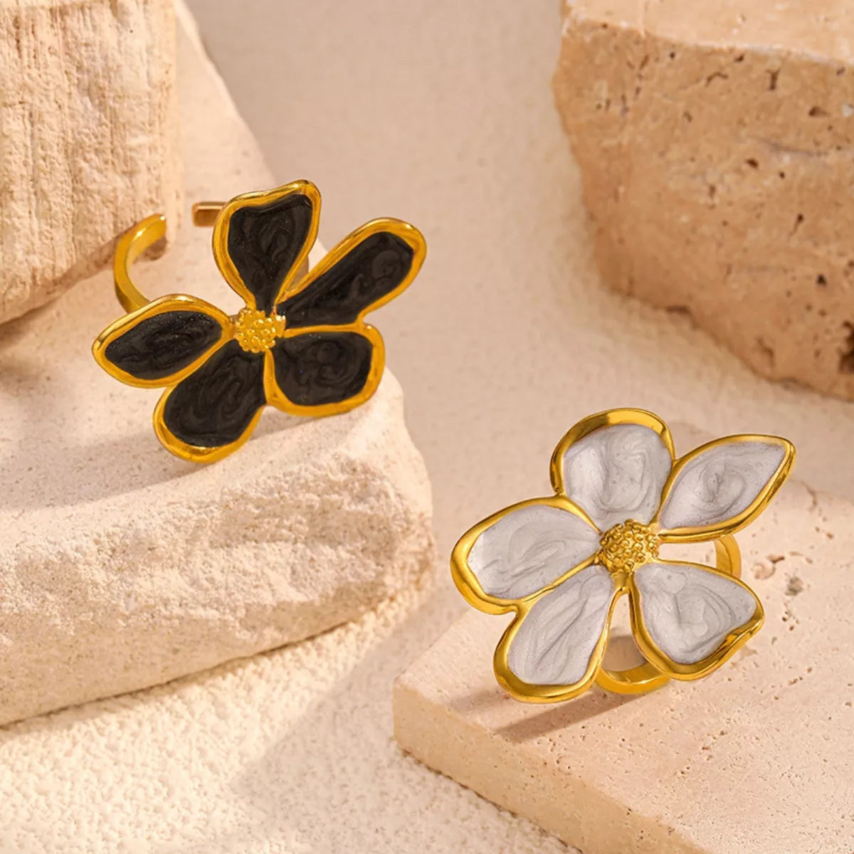 Pair of gold-tone open flower rings with black and white petals on a stone block