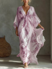 Pale pink and purple feather-print maxi dress with loose sleeves and a tied V-neckline.