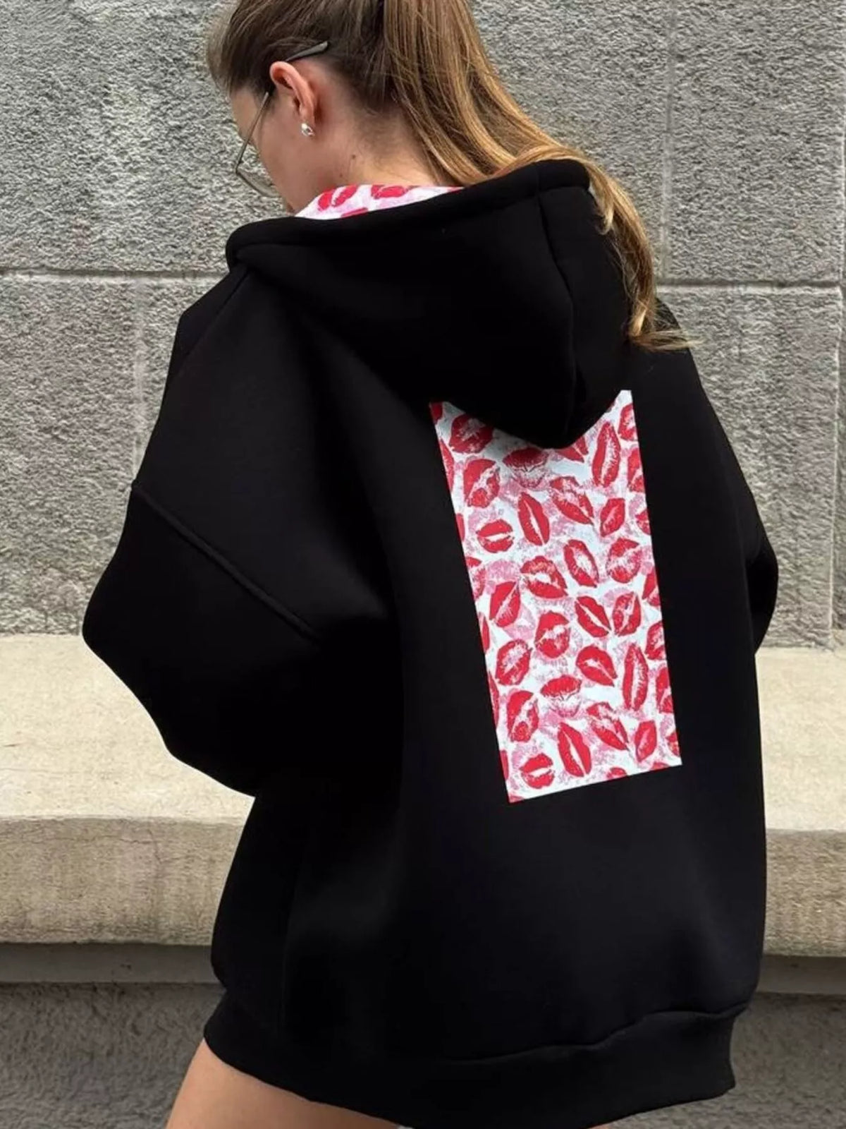 Close back view of black hoodie highlighting its large red lip-print panel