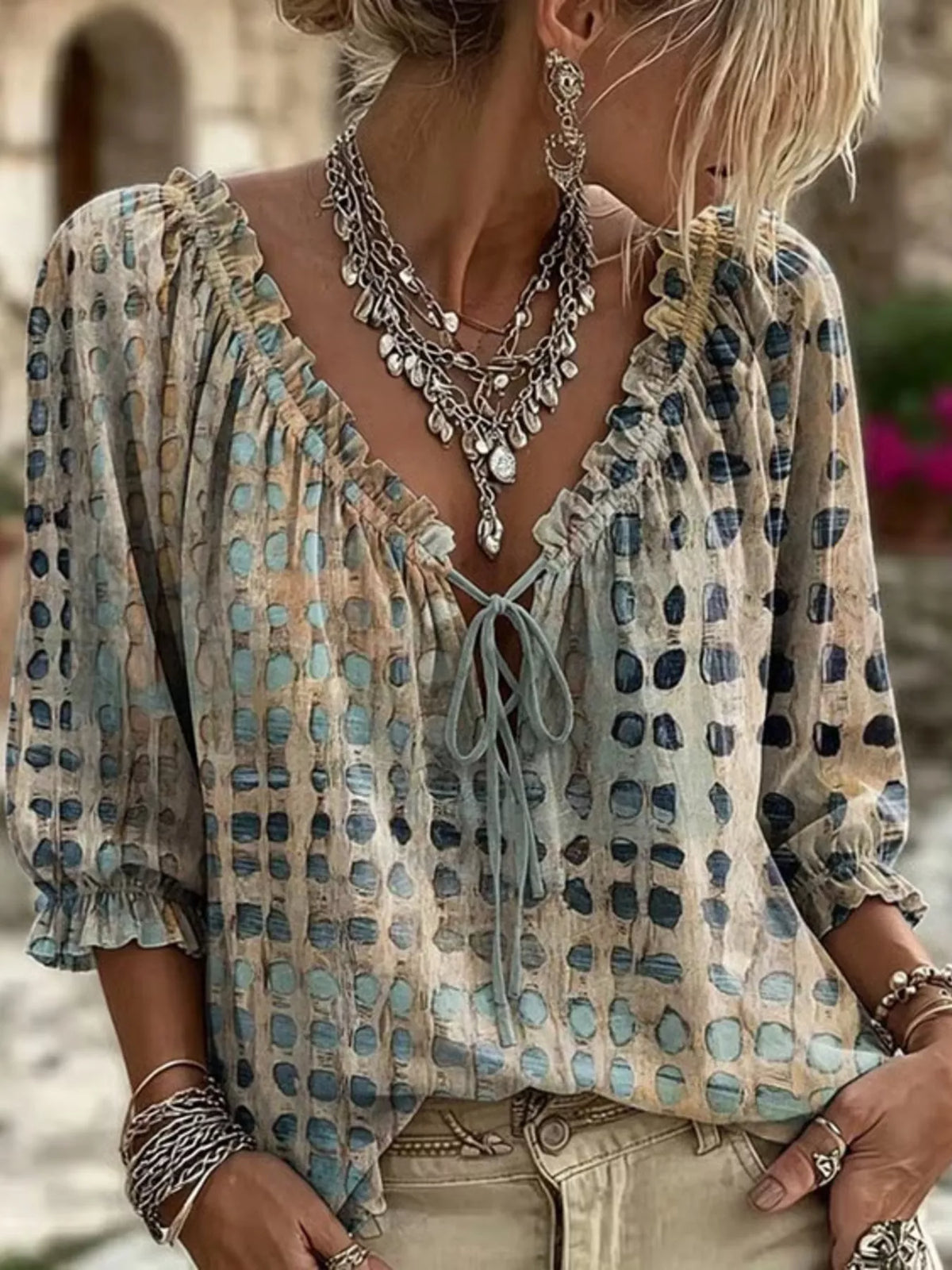 Model wearing a beige blouse with blue and charcoal spots, ruffled V-neck tie and three-quarter sleeves