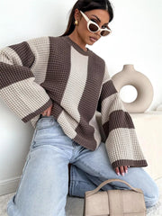 Model sitting in cream and taupe oversized sweater with one knee raised