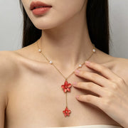 Gold-tone pearl necklace with red flower drops worn with a light top