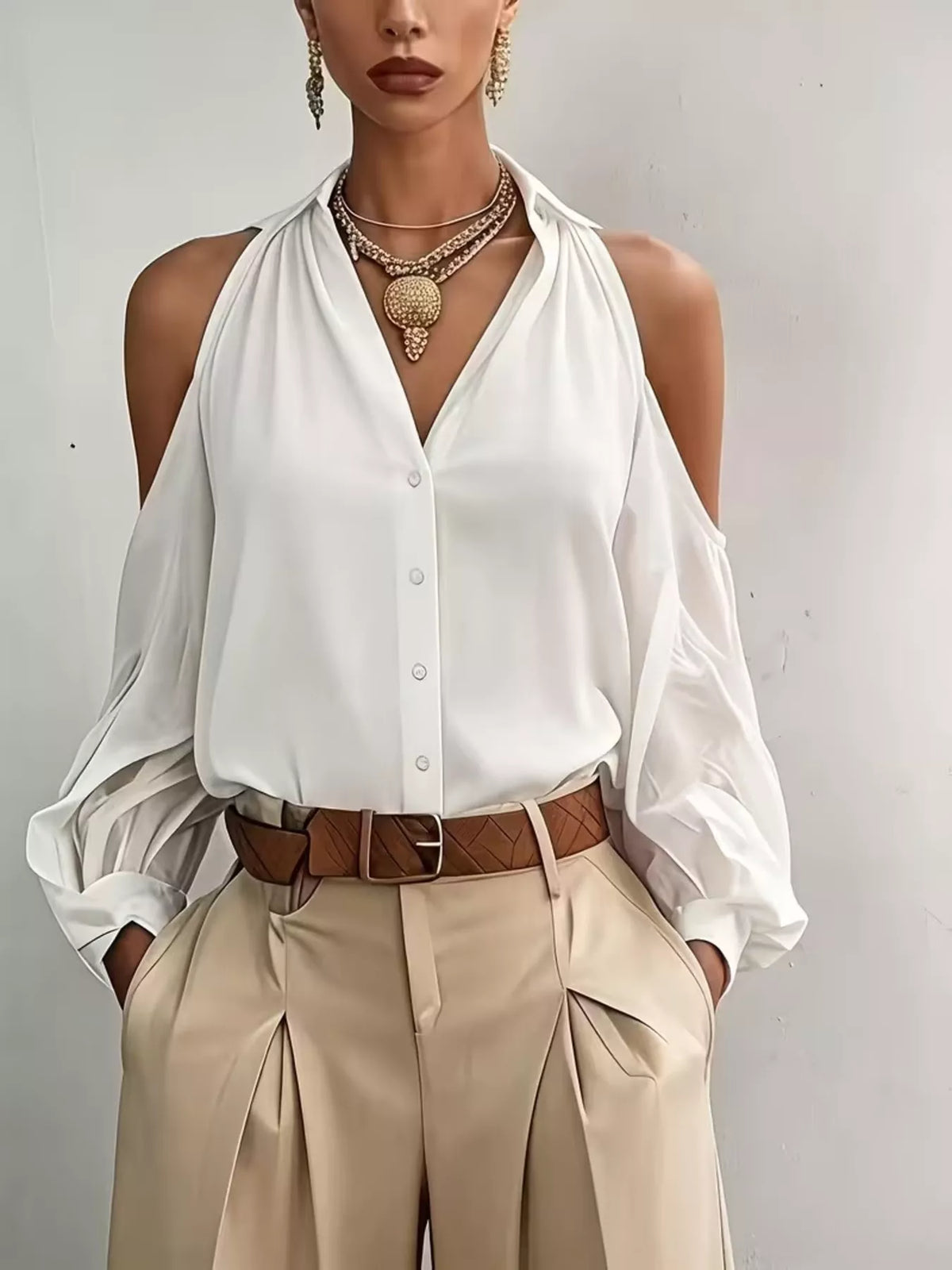 Model in white cold-shoulder button-front blouse with beige trousers.