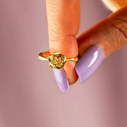 Gold rose ring held between fingers with a pink manicure