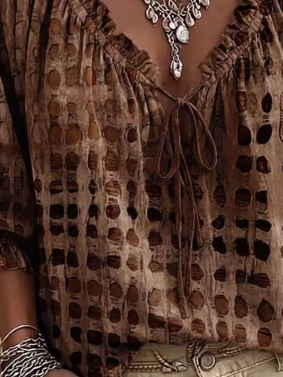 Close-up of brown blouse with spotted pattern, ruffle trim and tie at the neckline