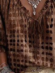 Close-up of brown blouse with spotted pattern, ruffle trim and tie at the neckline