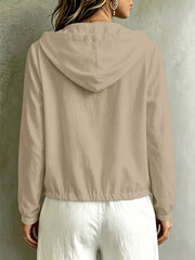 Back view of the beige hooded blouse with its gathered drawstring hem.