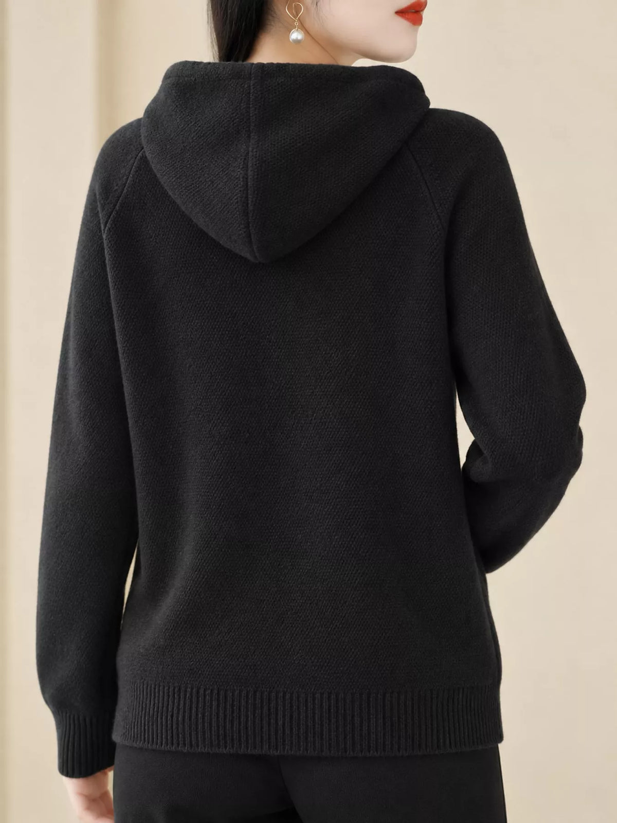 Back view of the black knit sweater showing its hood and ribbed hem.