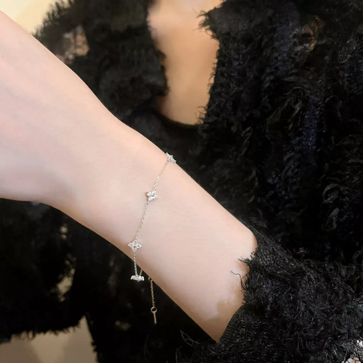 Close view of the dainty silver bracelet worn on a wrist beside a dark sleeve.