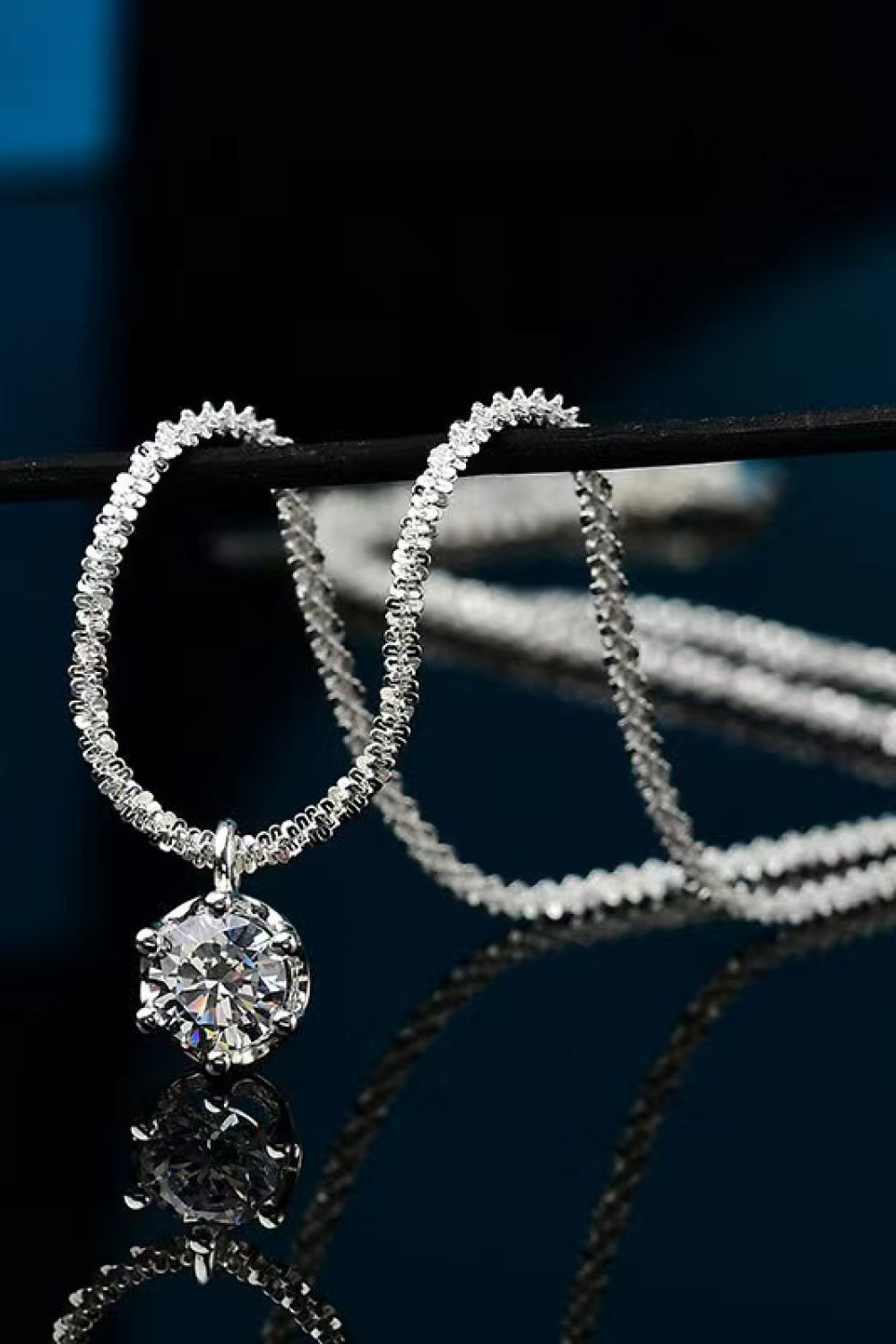 Silver-tone pendant necklace draped in loops over a bar on a reflective dark surface