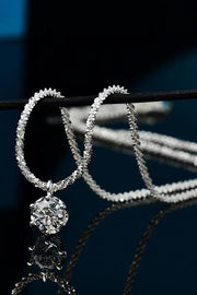 Silver-tone pendant necklace draped in loops over a bar on a reflective dark surface