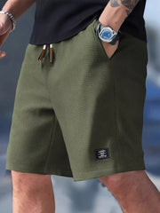 Model wearing olive green waffle-textured drawstring shorts with one hand in a pocket