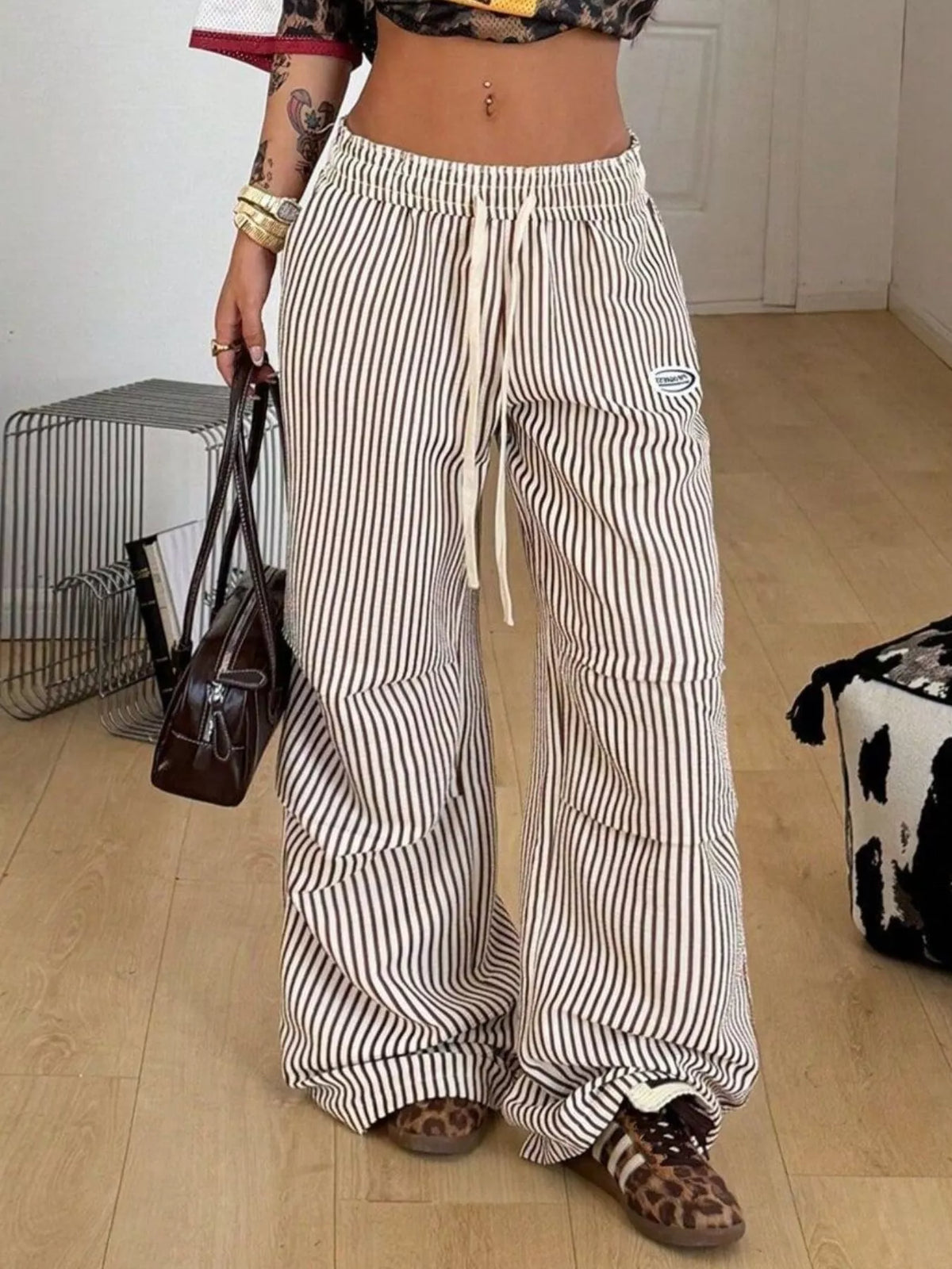 Front view of striped pants with wide legs and drawstring waist, model carrying a bag