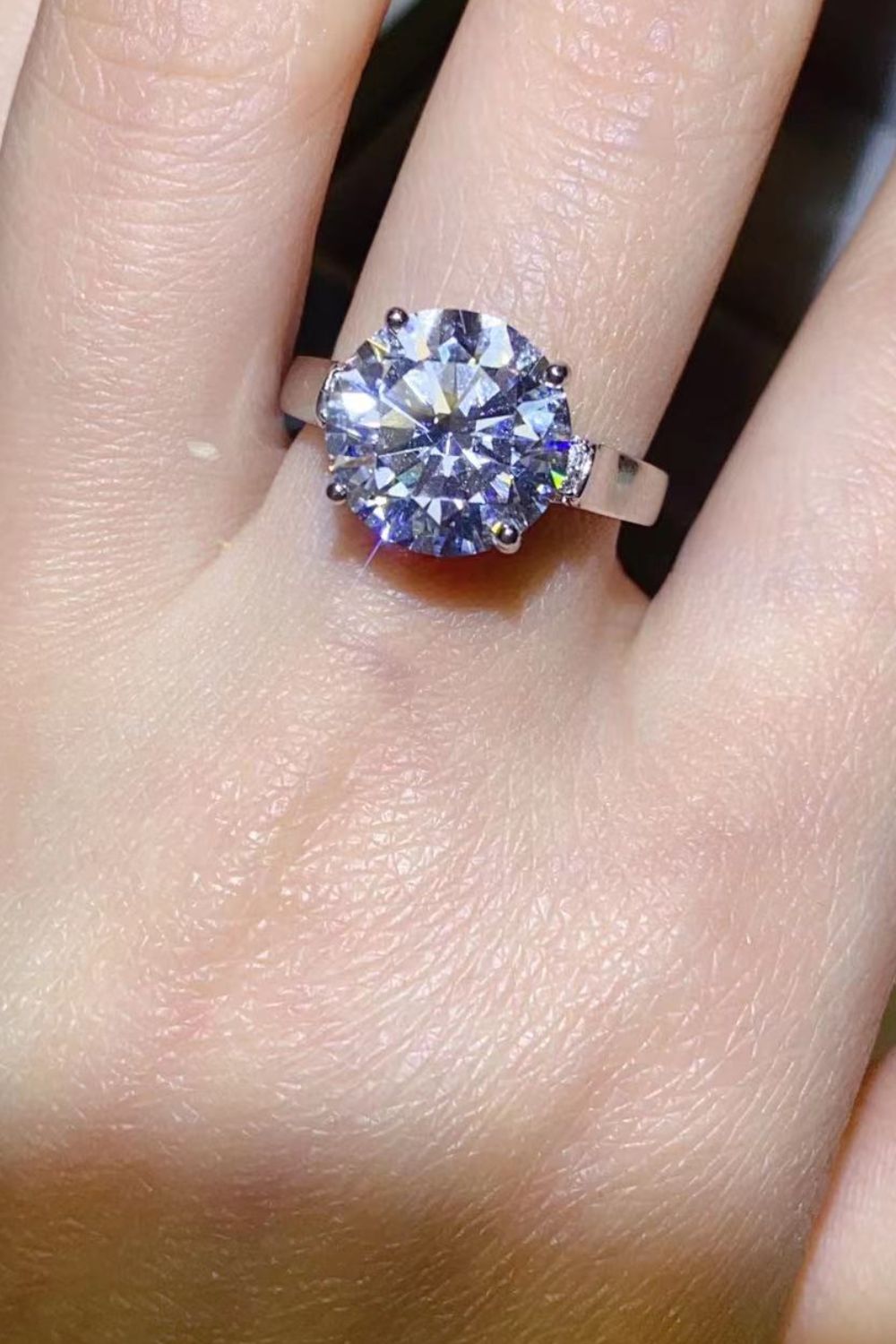 Large round moissanite solitaire ring worn on a hand, viewed from above.