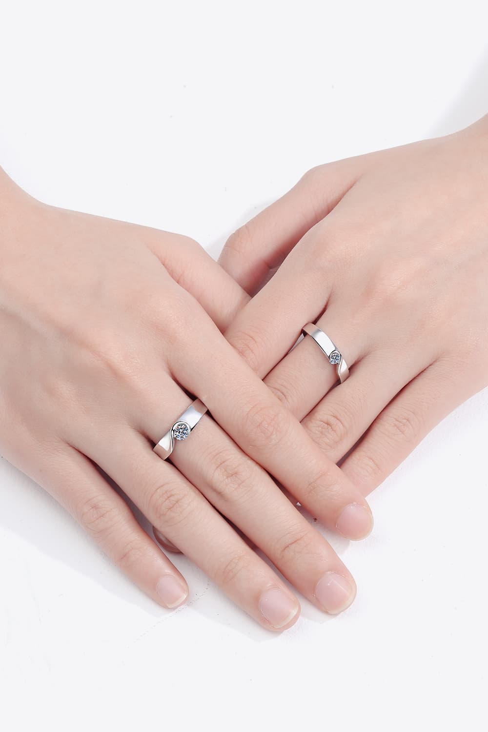 Two rhodium-plated moissanite rings worn on hands against a white background.