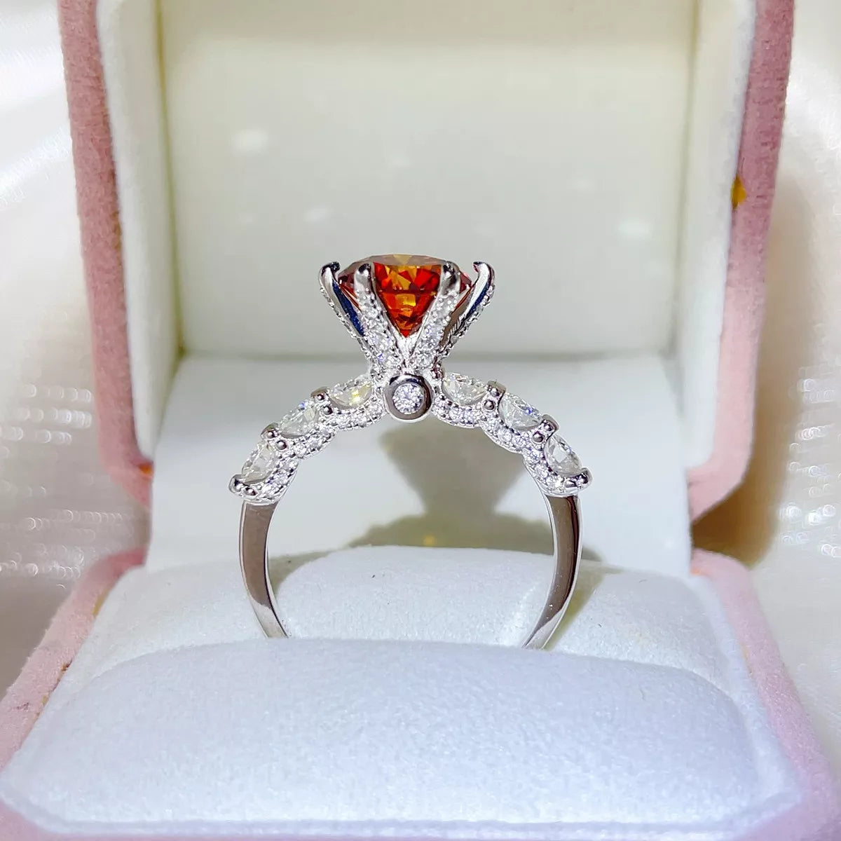 Front view of a three-carat red-orange moissanite ring in an open white box