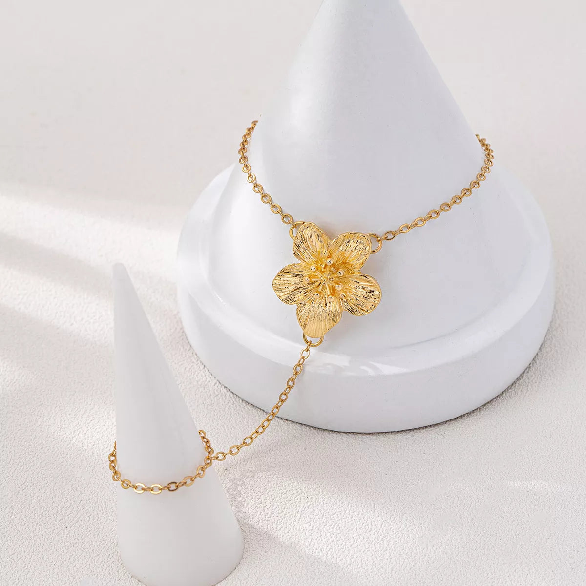 Gold-tone flower hand chain bracelet displayed on jewelry stand