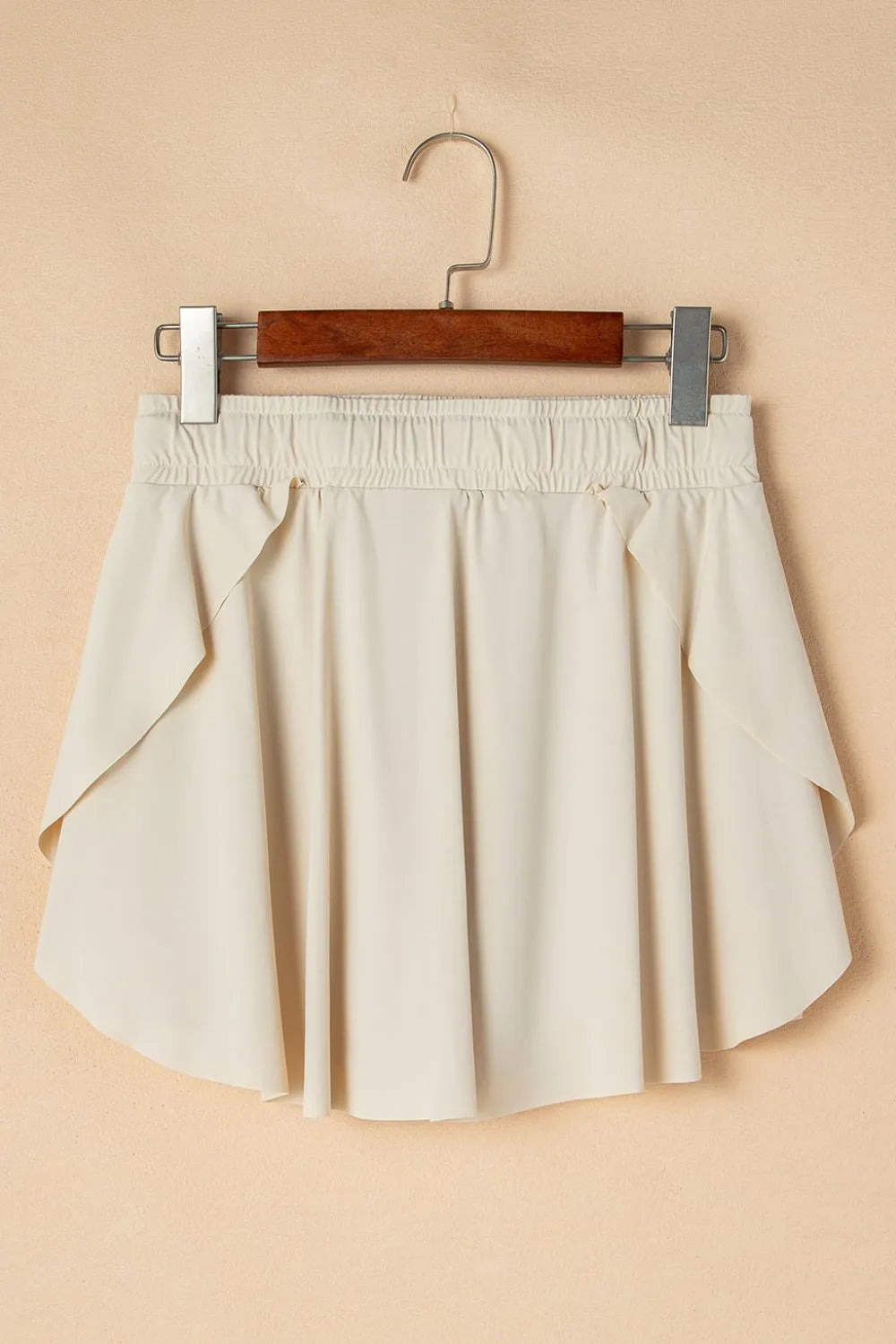 Ivory skort hanging against a beige wall, front view.