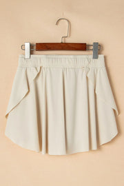Ivory skort hanging against a beige wall, front view.