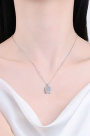 Model wearing a small rectangular pendant necklace with a white neckline