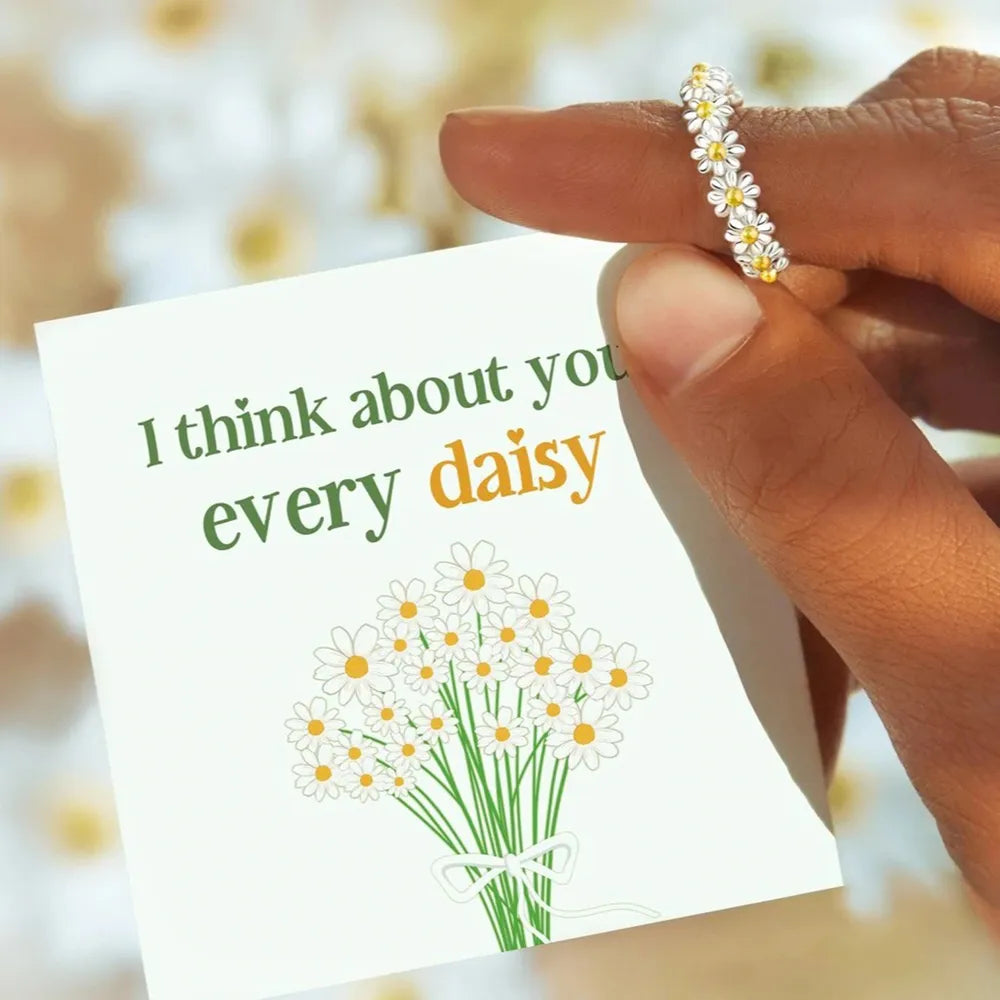 Close-up of daisy flower band ring beside floral message card