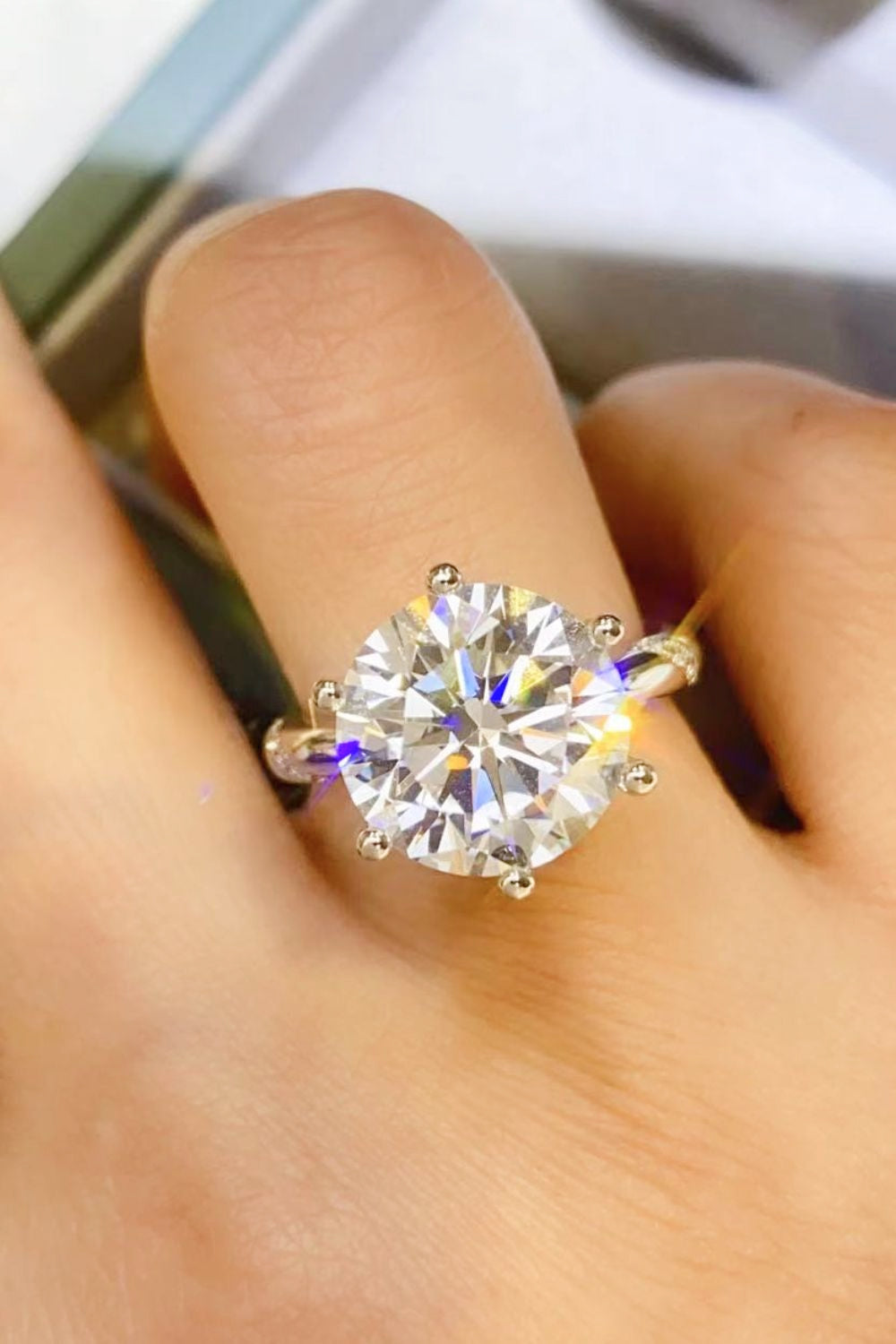 Close-up of a round six-prong moissanite ring worn on a finger.