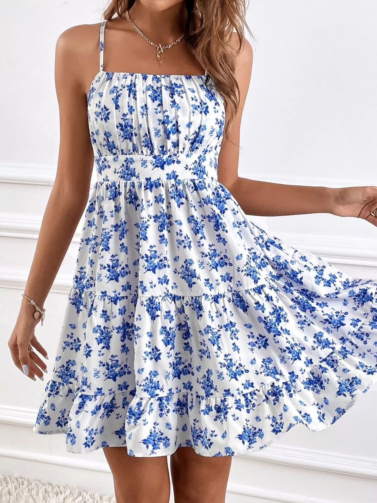 Model holding out the tiered skirt of a white spaghetti-strap mini dress with blue floral print
