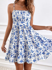 Model holding out the tiered skirt of a white spaghetti-strap mini dress with blue floral print