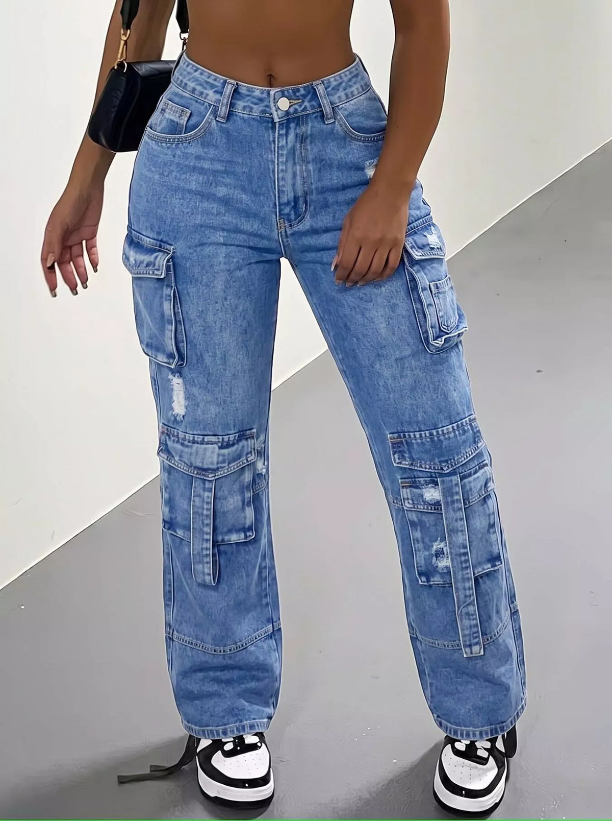 Front view of blue distressed cargo jeans showing multiple leg pockets and black-and-white trainers