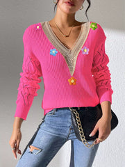 Pink V-neck sweater with beige trim and colourful flower appliqués, standing view.