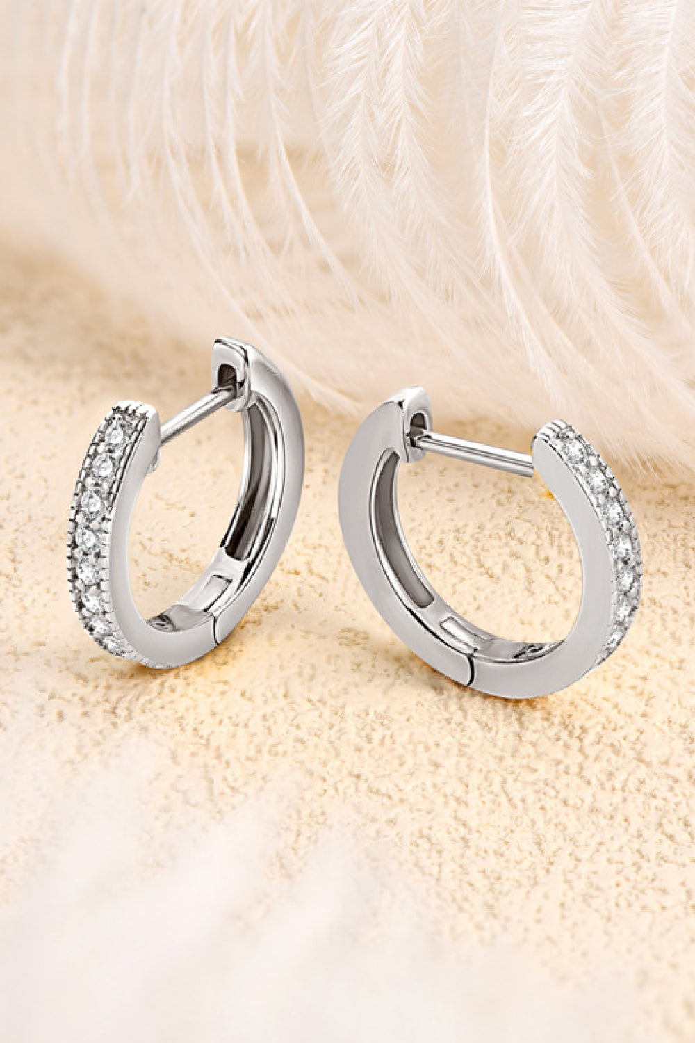 Pair of stone-set silver hoop earrings displayed open against a soft textured background