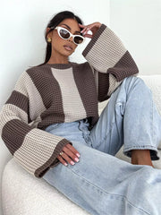Seated model wearing cream and taupe colour-block sweater with wide sleeves and light jeans