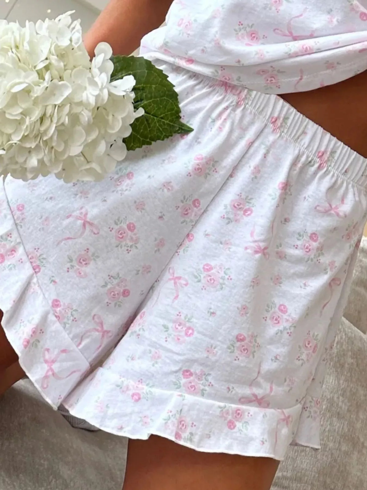 Close-up of white lounge shorts showing pale pink print, elastic waist and ruffled hem