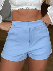 Model wearing light-blue high-waisted tailored shorts with white crop top
