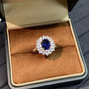 Close view of a royal-blue oval sapphire ring with a clear-stone halo in its open box