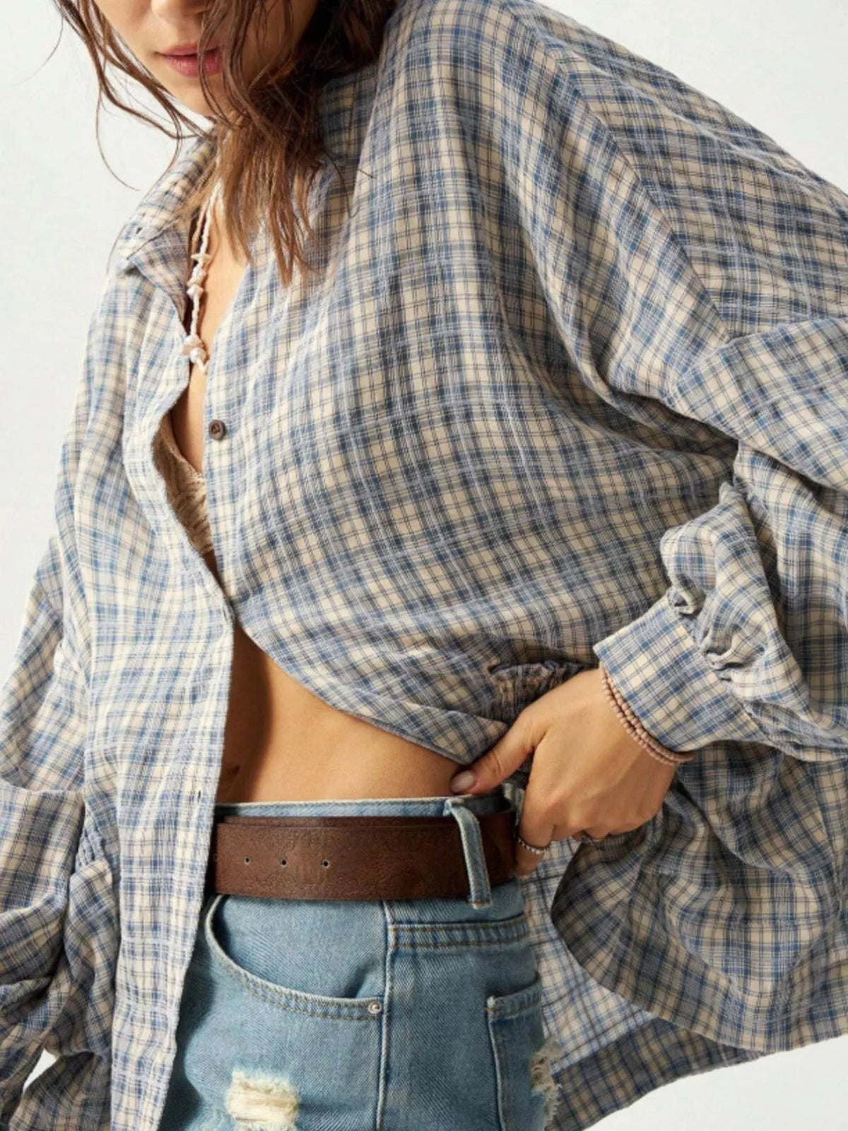 Close view of blue plaid shirt front and roomy sleeve with hand at waistband