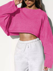 Model wearing a bright pink oversized cropped sweatshirt with long sleeves, front view