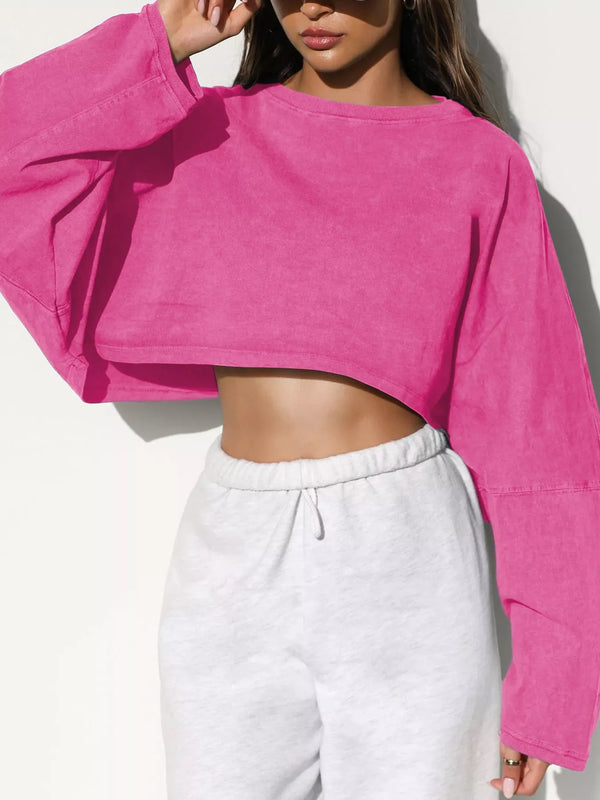 Model wearing a bright pink oversized cropped sweatshirt with long sleeves, front view