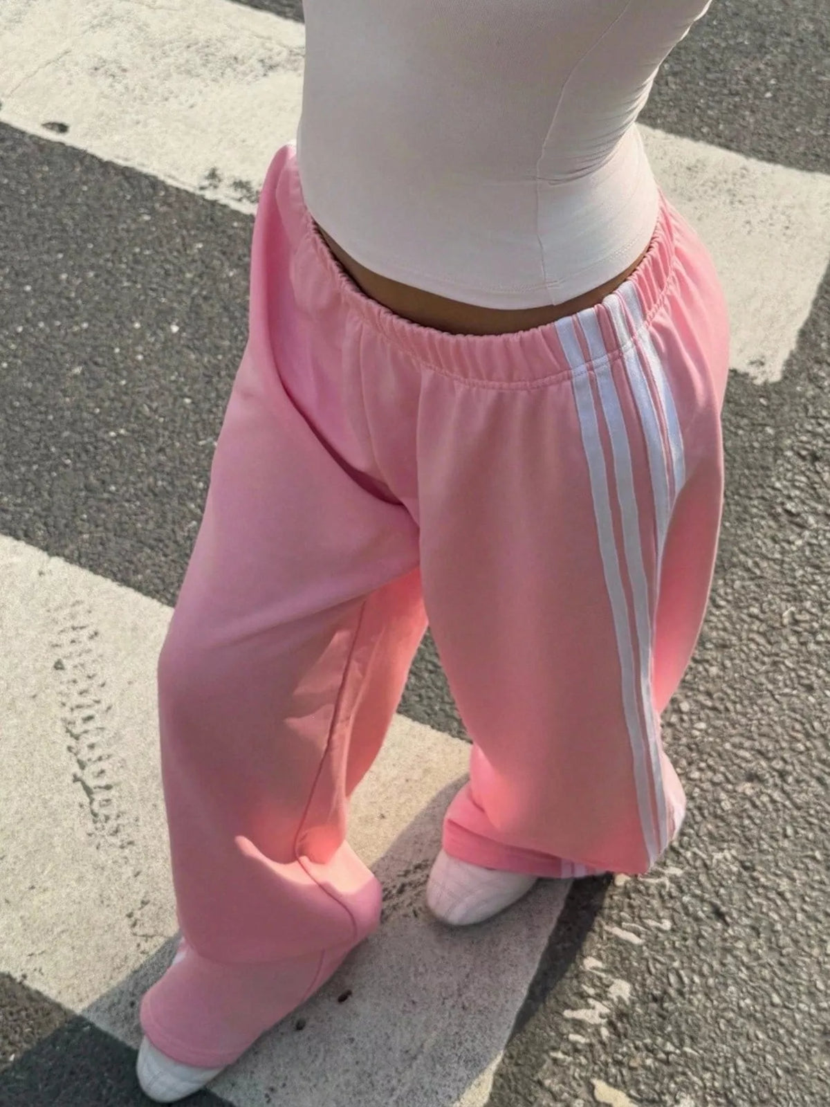 Pink track pants with elastic waist and white side stripes, angled view