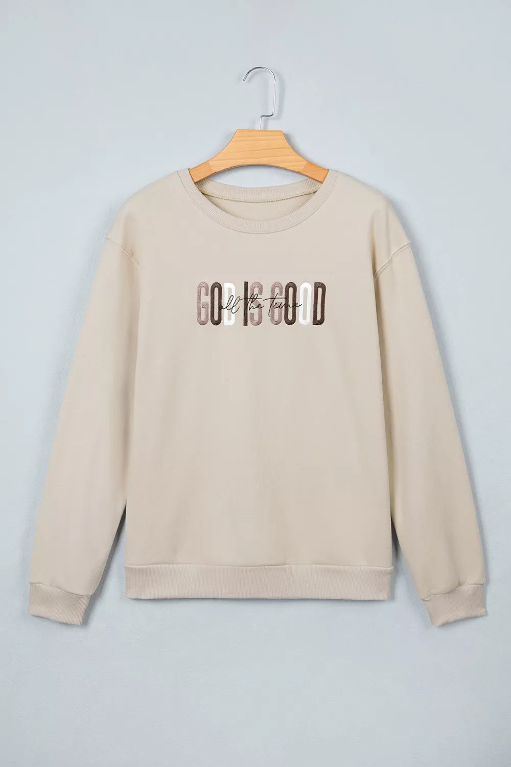 Beige God Is Good graphic crew-neck sweatshirt displayed from the front on a hanger